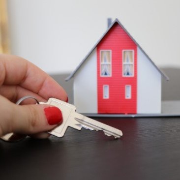 Hausmiete - Hand mit Schlüssel vor rot-weißem Miniaturhaus