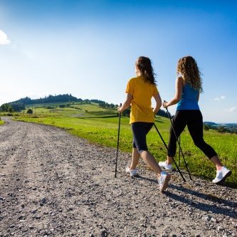 Zwei junge Frauen beim Nordic Walking auf einem geschotterten Feldweg durch die Rhön