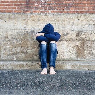 Jugendprobleme - Jugendlicher deprimiert sitzend vor einer Ziegelmauer