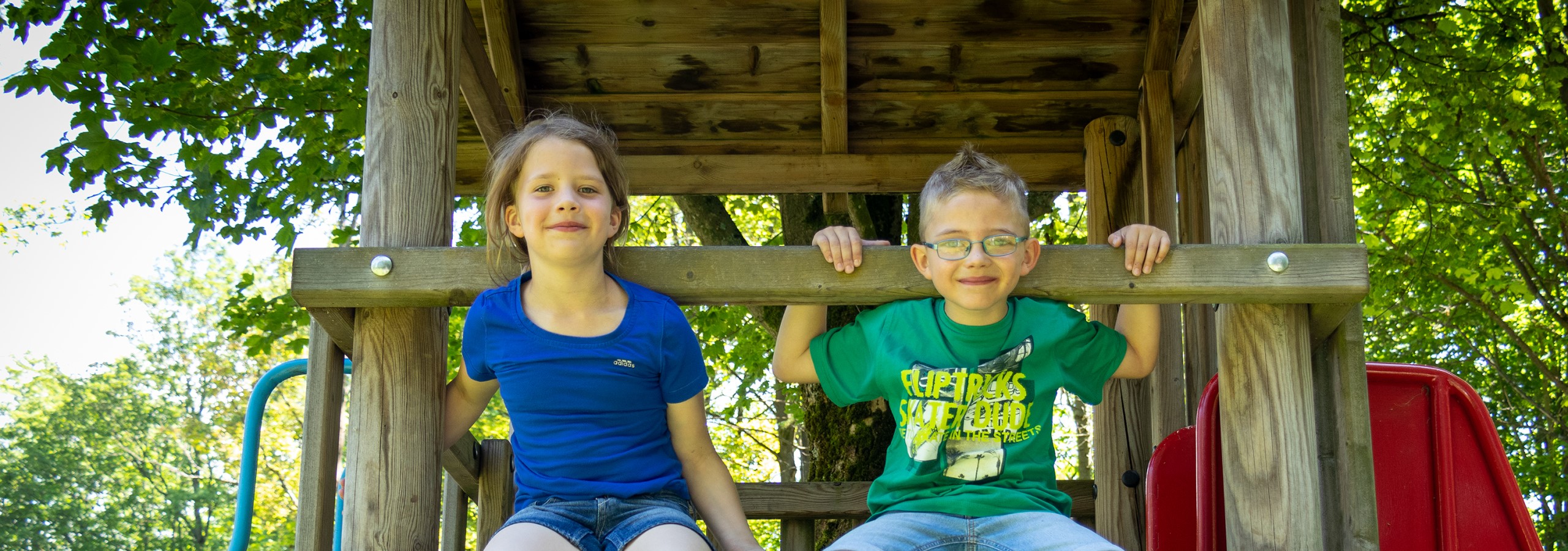 Familien und Kinder - Panoramaschnitt Junge und Mädchen auf Rutschenturm lächeln in die Kamera