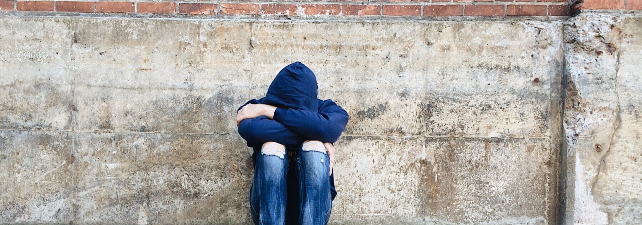 Jugendprobleme - Panoramaschnitt Jugendlicher deprimiert sitzend vor einer Ziegelmauer