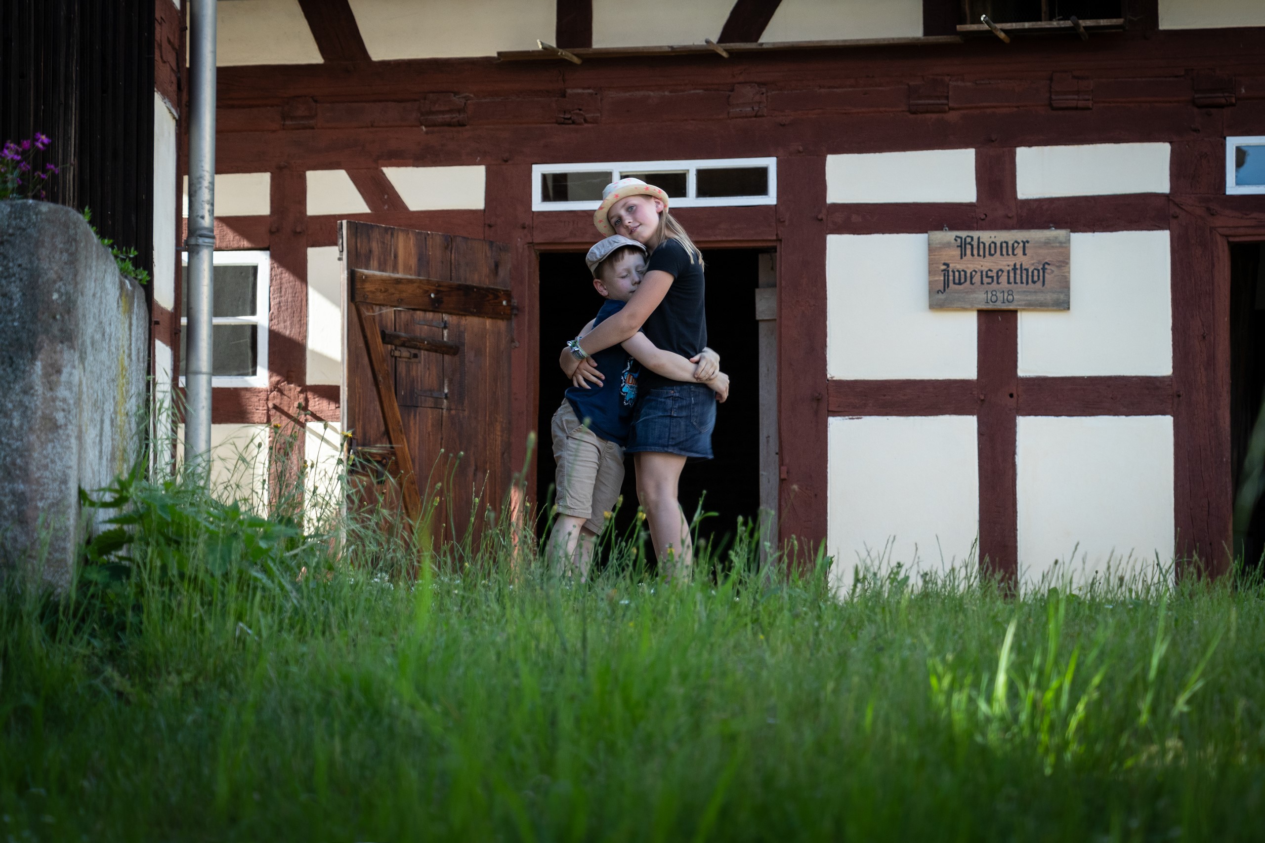 2 Kinder herzen sich vor der Kulisse des 2-seit-Hofes im Tanner Museumsdorf